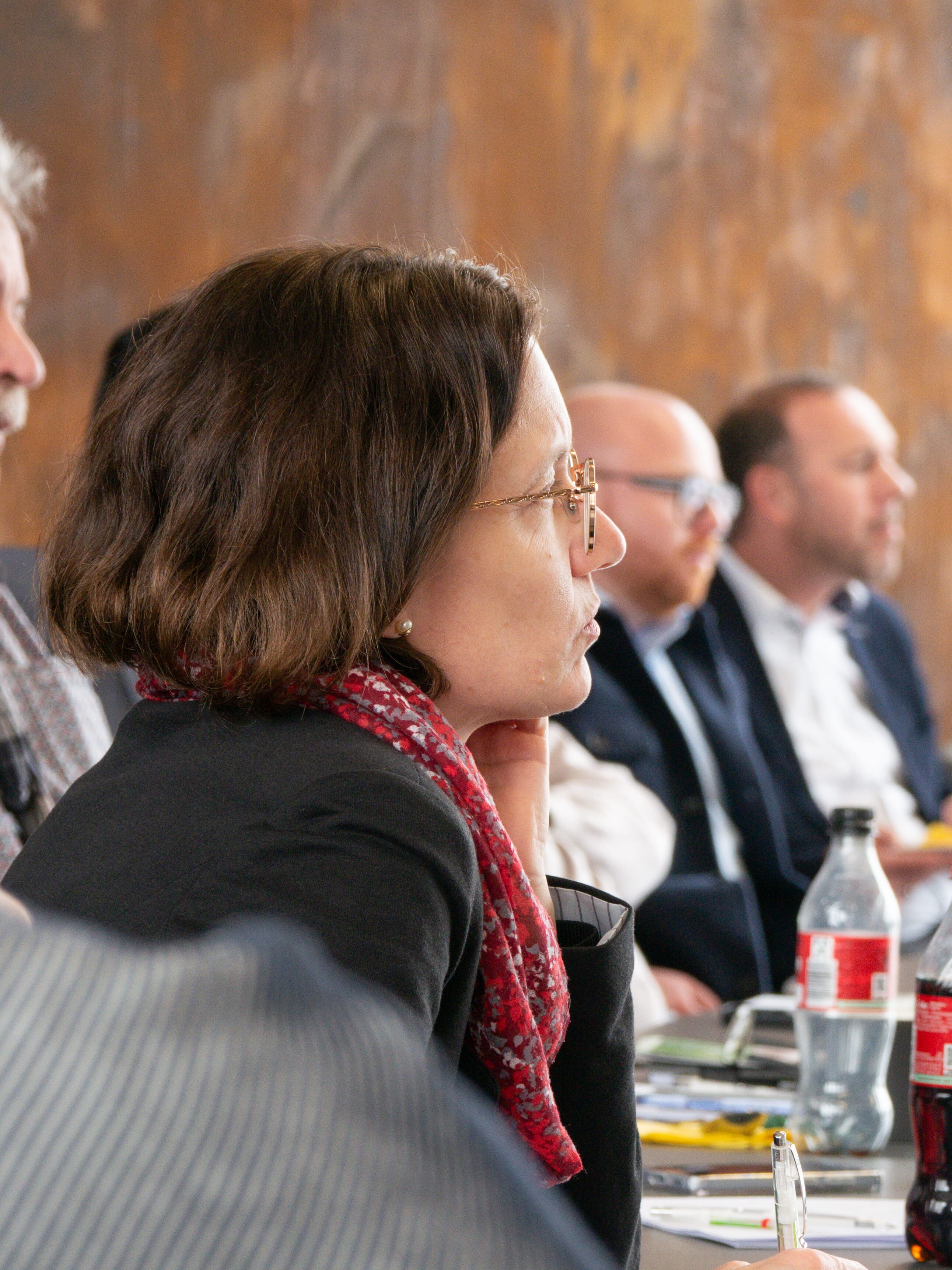 Erfolgsrezepte für Morgen Eine Frau sitzt an einem Tisch mit einem Stift, umgeben von einer Gruppe von Menschen.