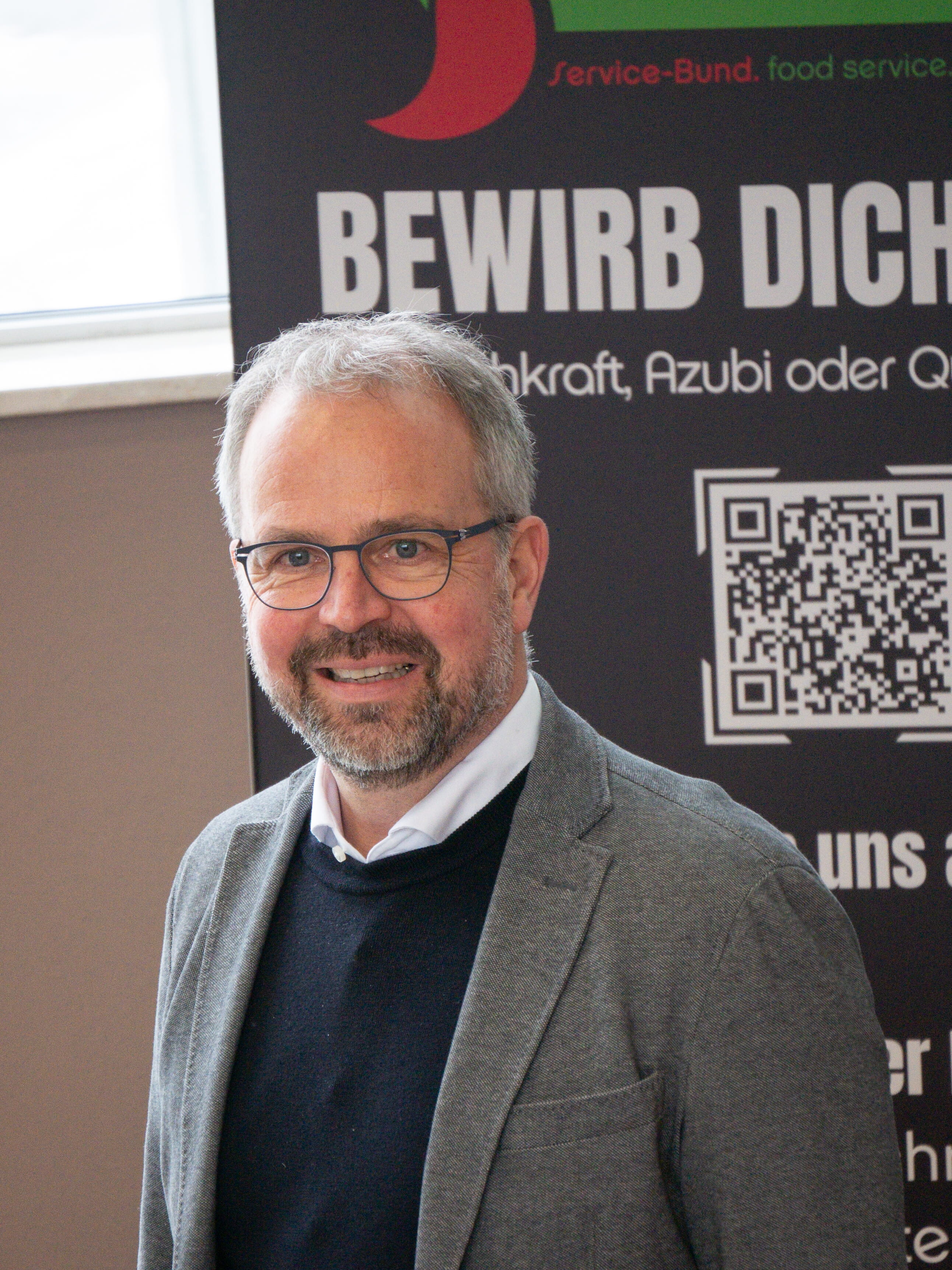 Erfolgsrezepte für Morgen Ein Mann mit Brille und grauem Blazer lächelt.