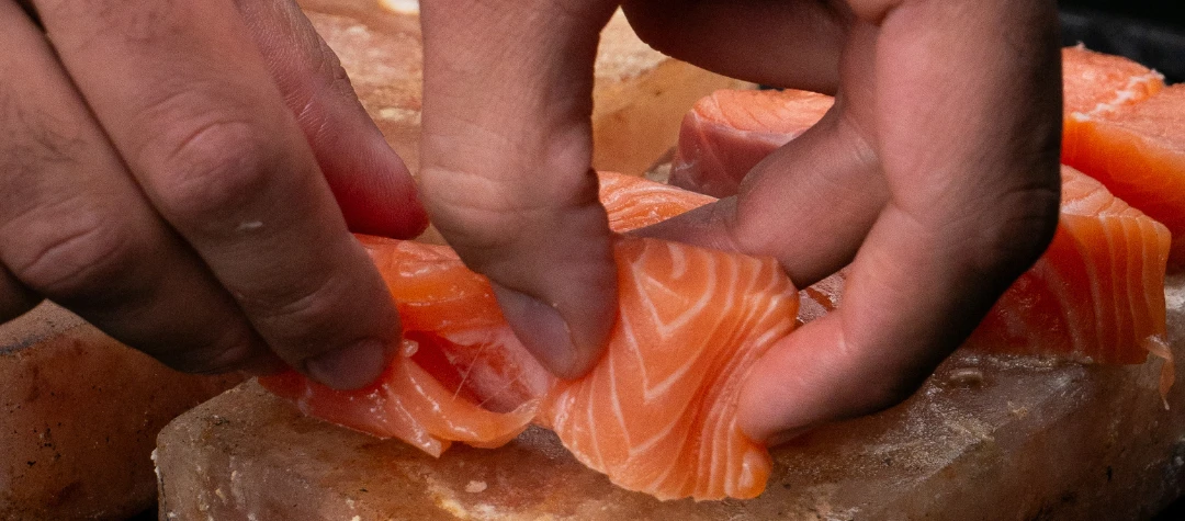 Eine Person kocht Lachs auf einem Salzstein vom Grill.