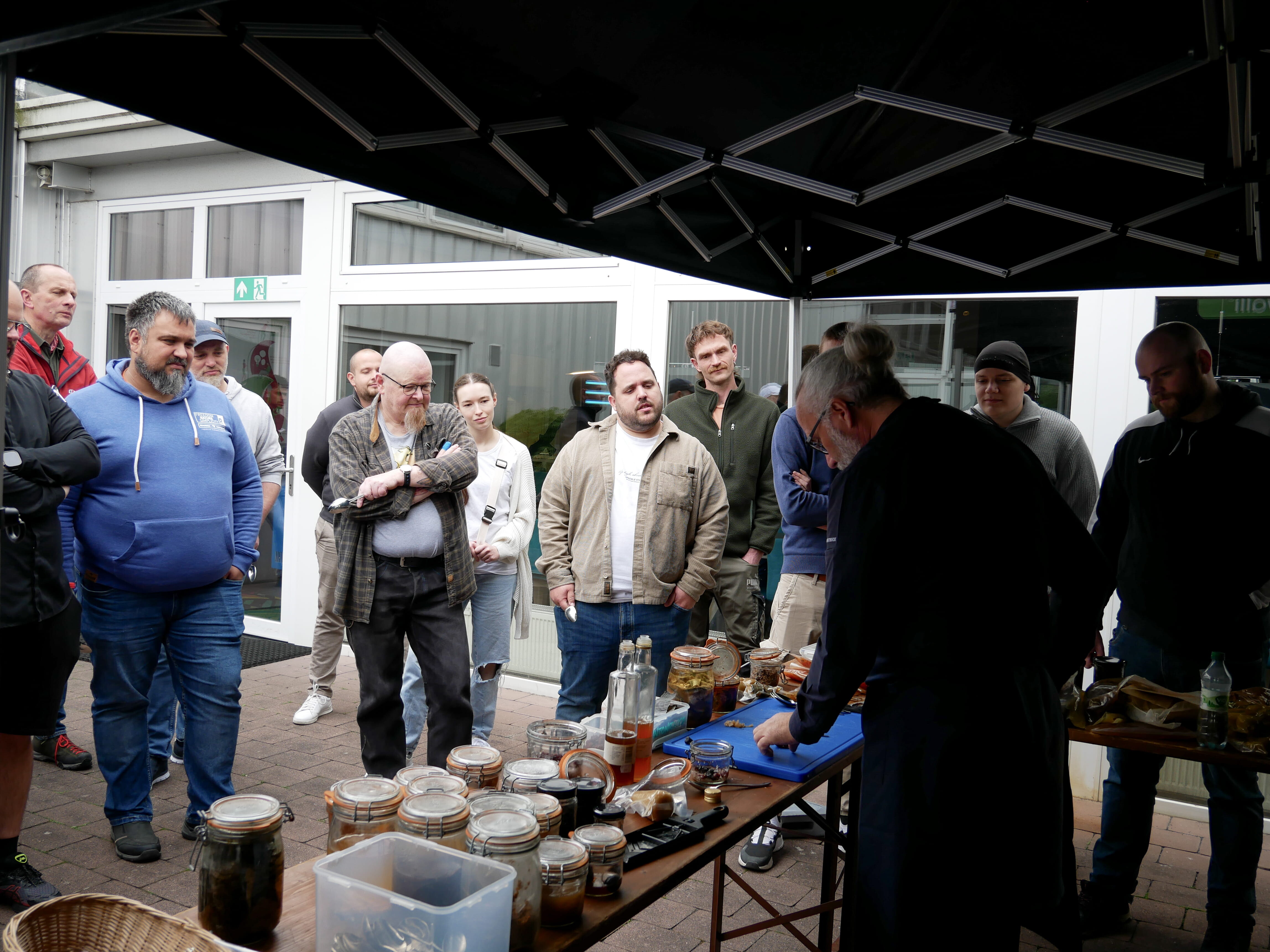 Fermentation & Umami Eine Gruppe von Menschen steht um einen Tisch mit Gläsern voller Lebensmittel.