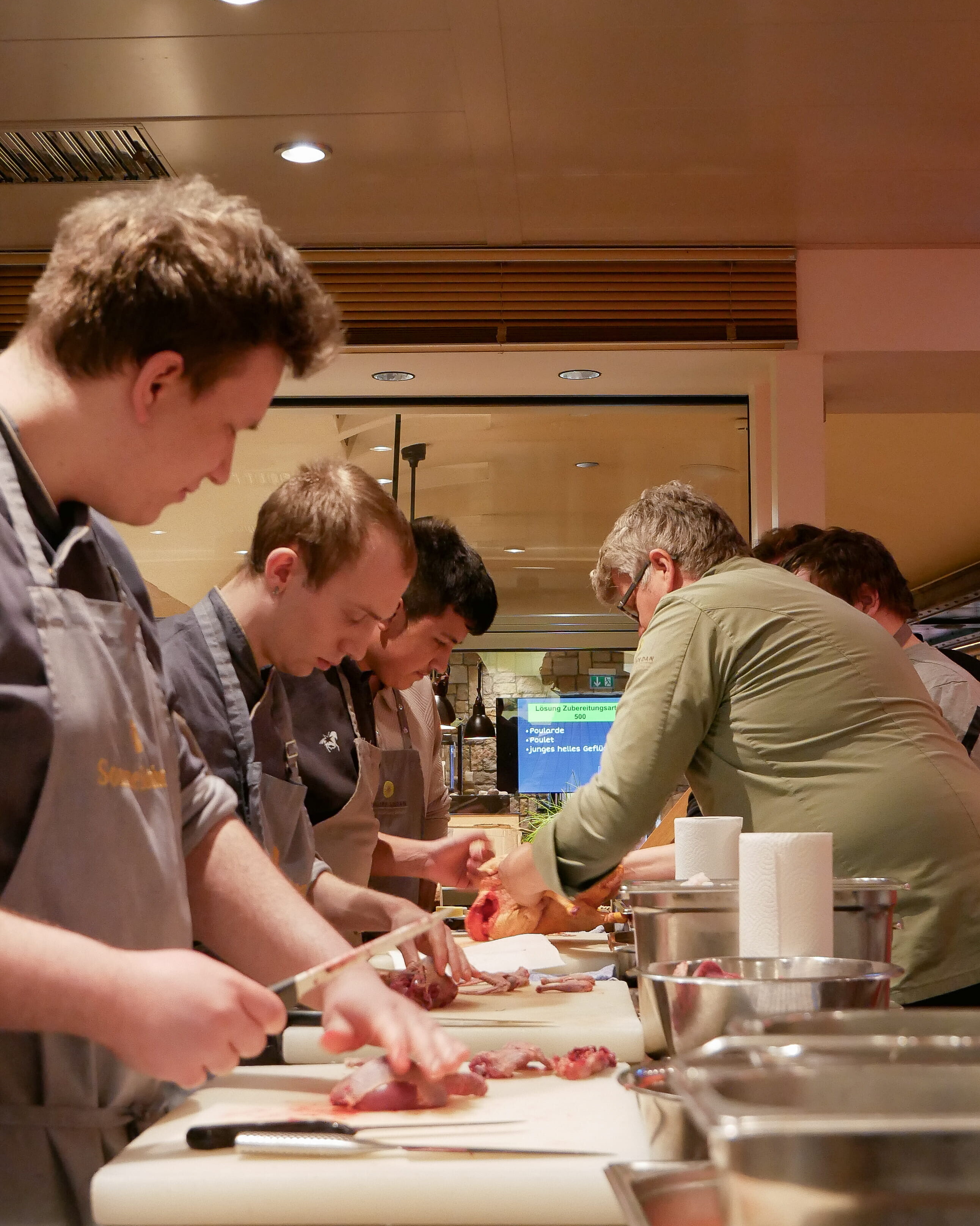 Eine Gruppe von Männern in Schürzen schneidet Fleisch.