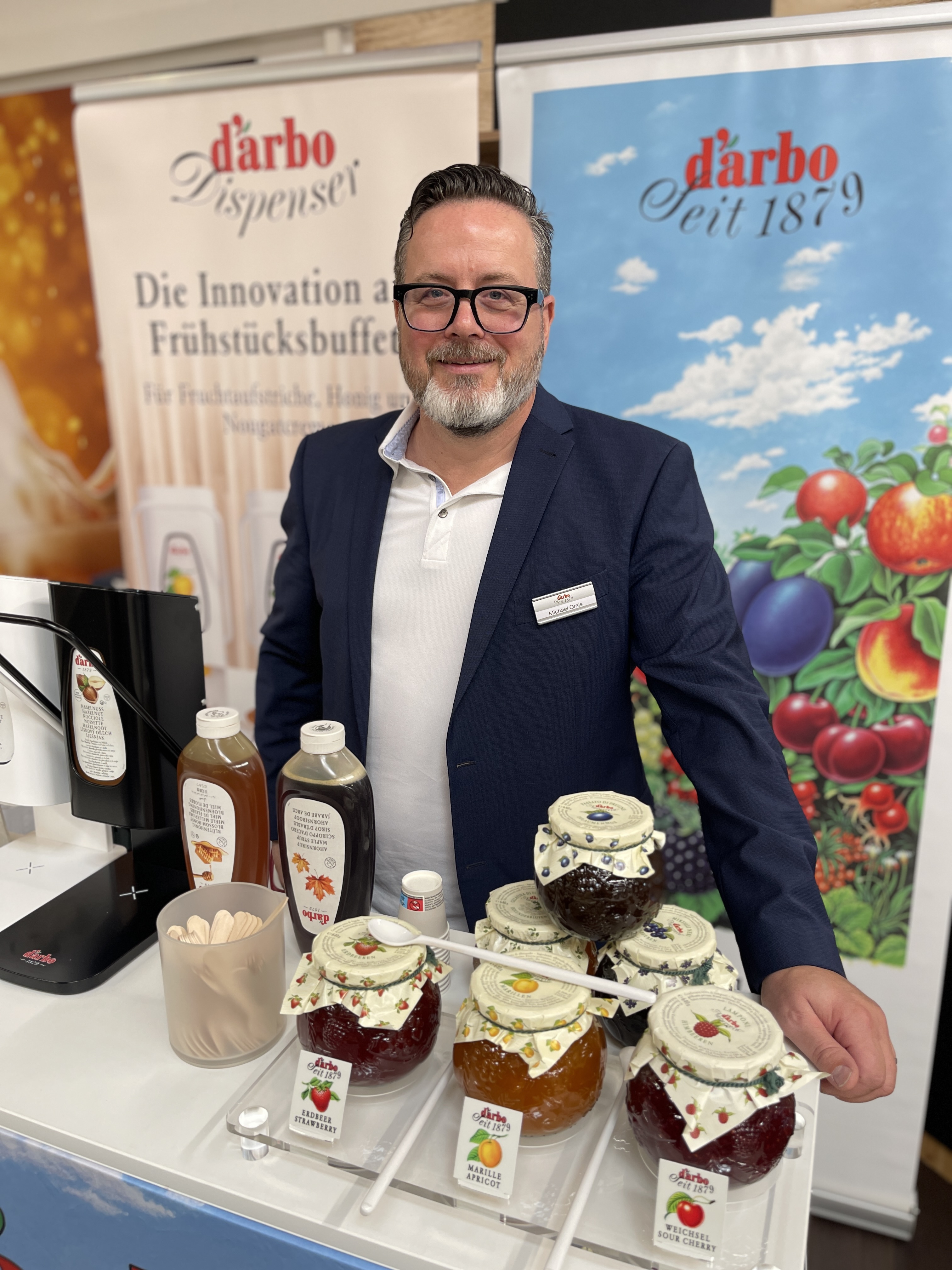 Ein Mann steht hinter einem Tresen mit Gläsern Marmelade.