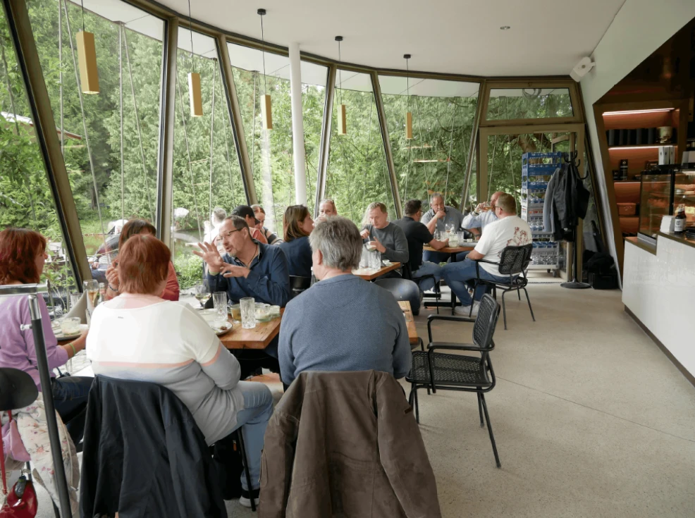 Sieben Bergen Kassel Eine Gruppe von Menschen sitzt an Tischen in einem Raum mit großen Fenstern.
