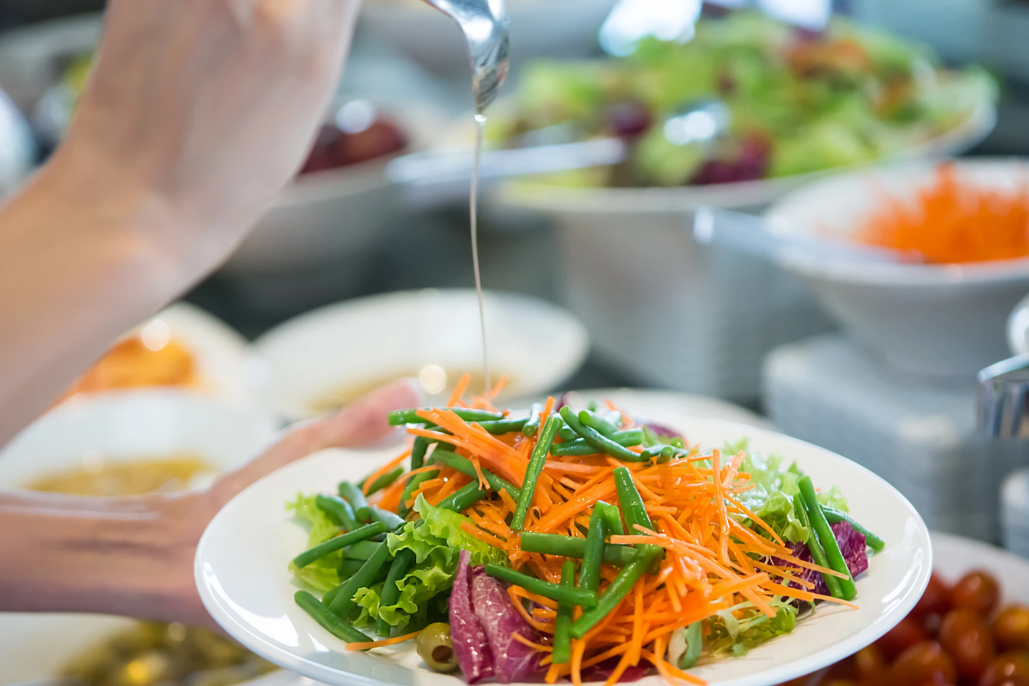 Nachhaltigkeit in der GV Eine Person gießt Olivenöl auf einen Teller mit Salat.