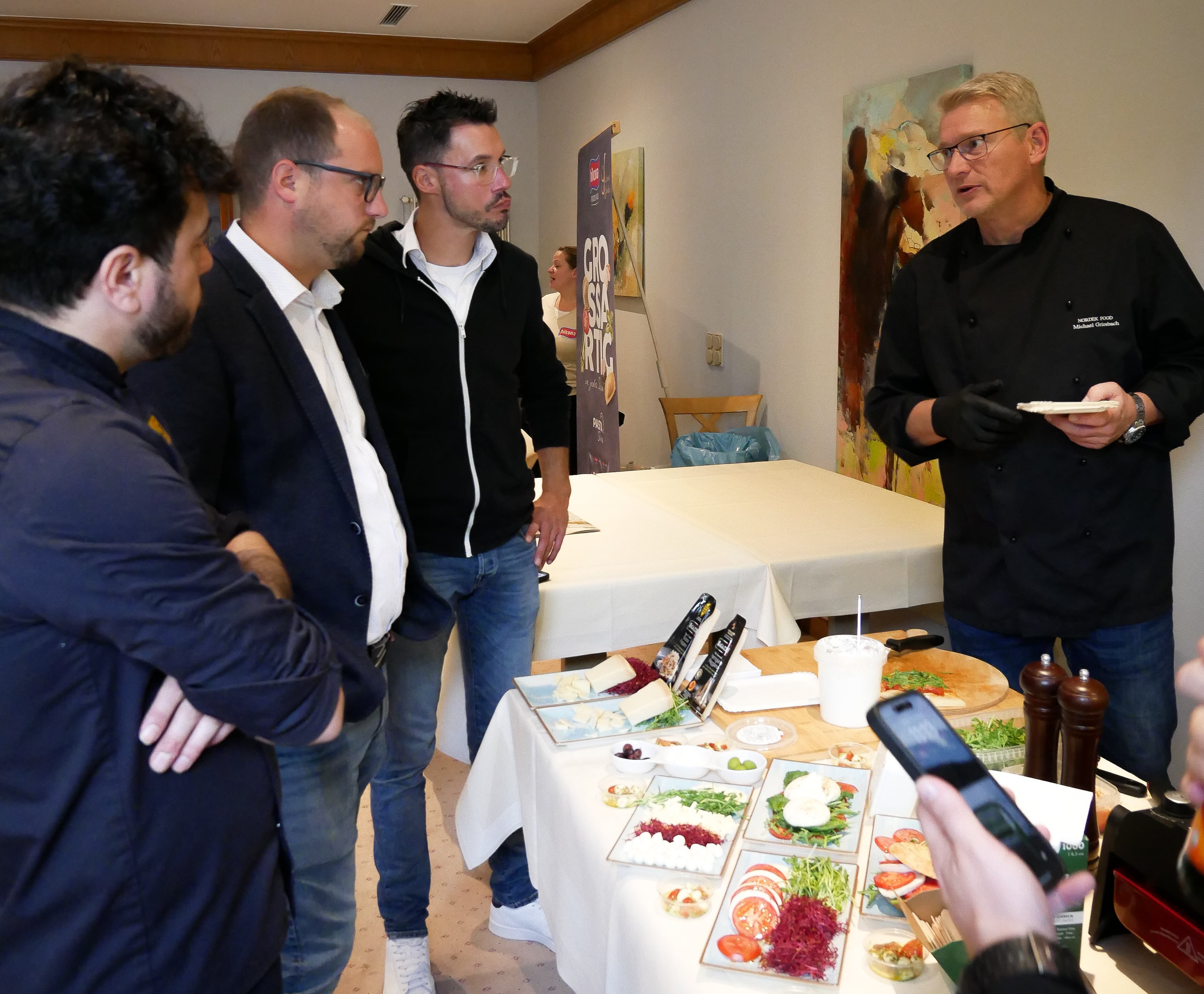 Lieferantenmeeting Oktober 2025 Eine Gruppe von Männern steht um einen Tisch mit Speisen.