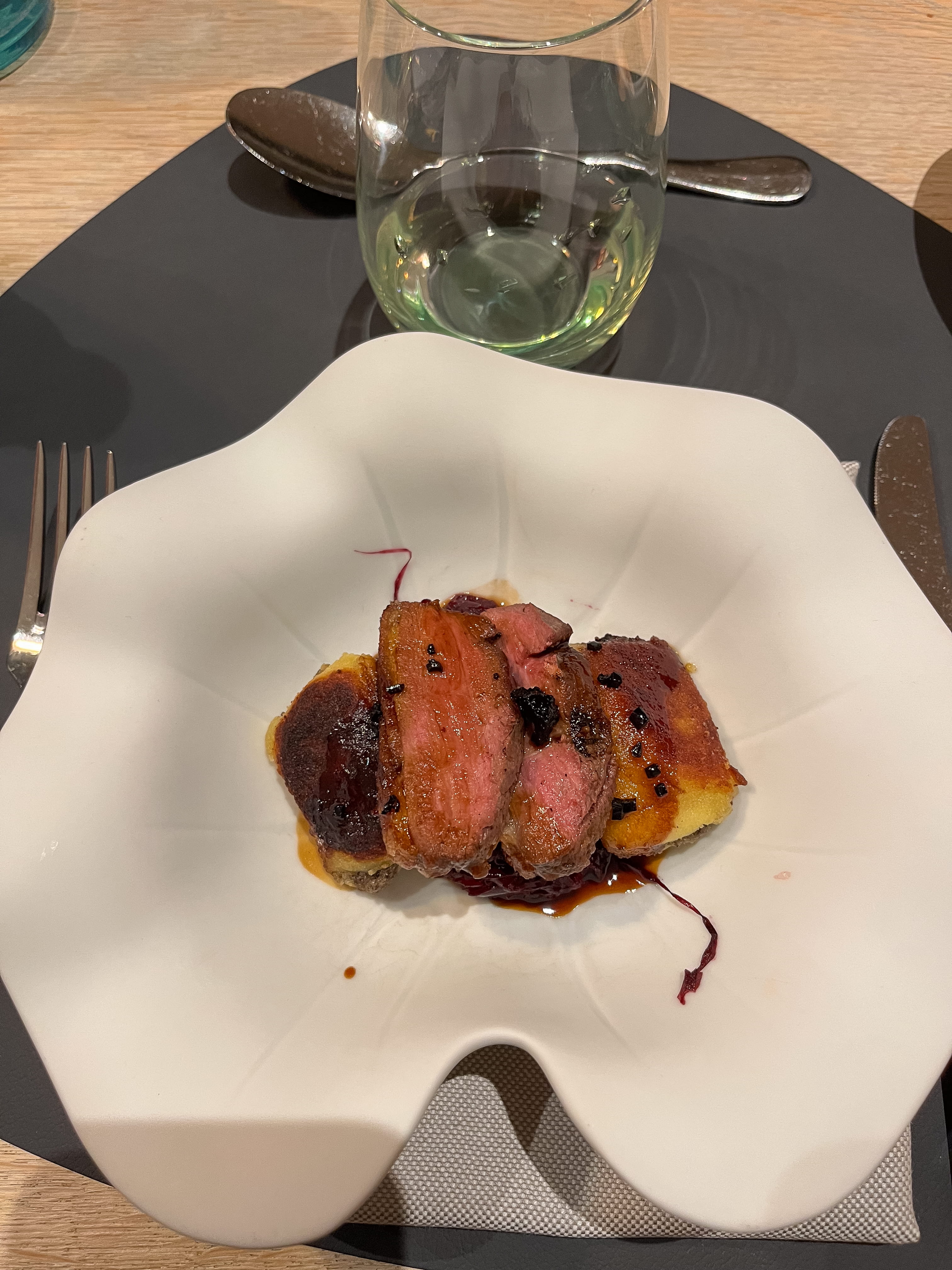 Ein Teller mit Essen auf einem Tisch, begleitet von einem Weinglas und Besteck.