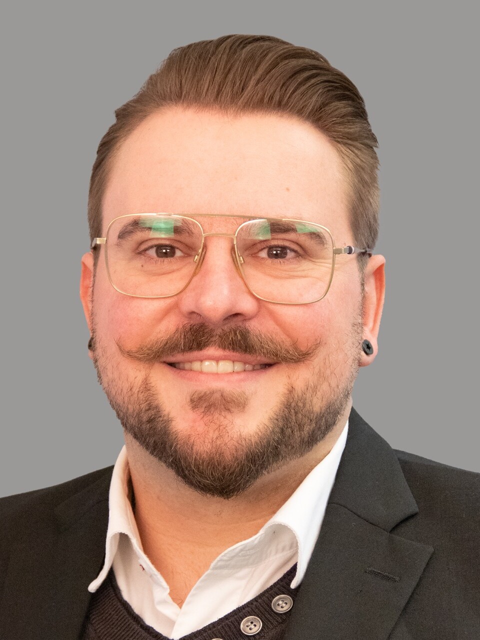 Tobias Gröschel Ein Mann mit Brille und Bart lächelt in einem Porträt.