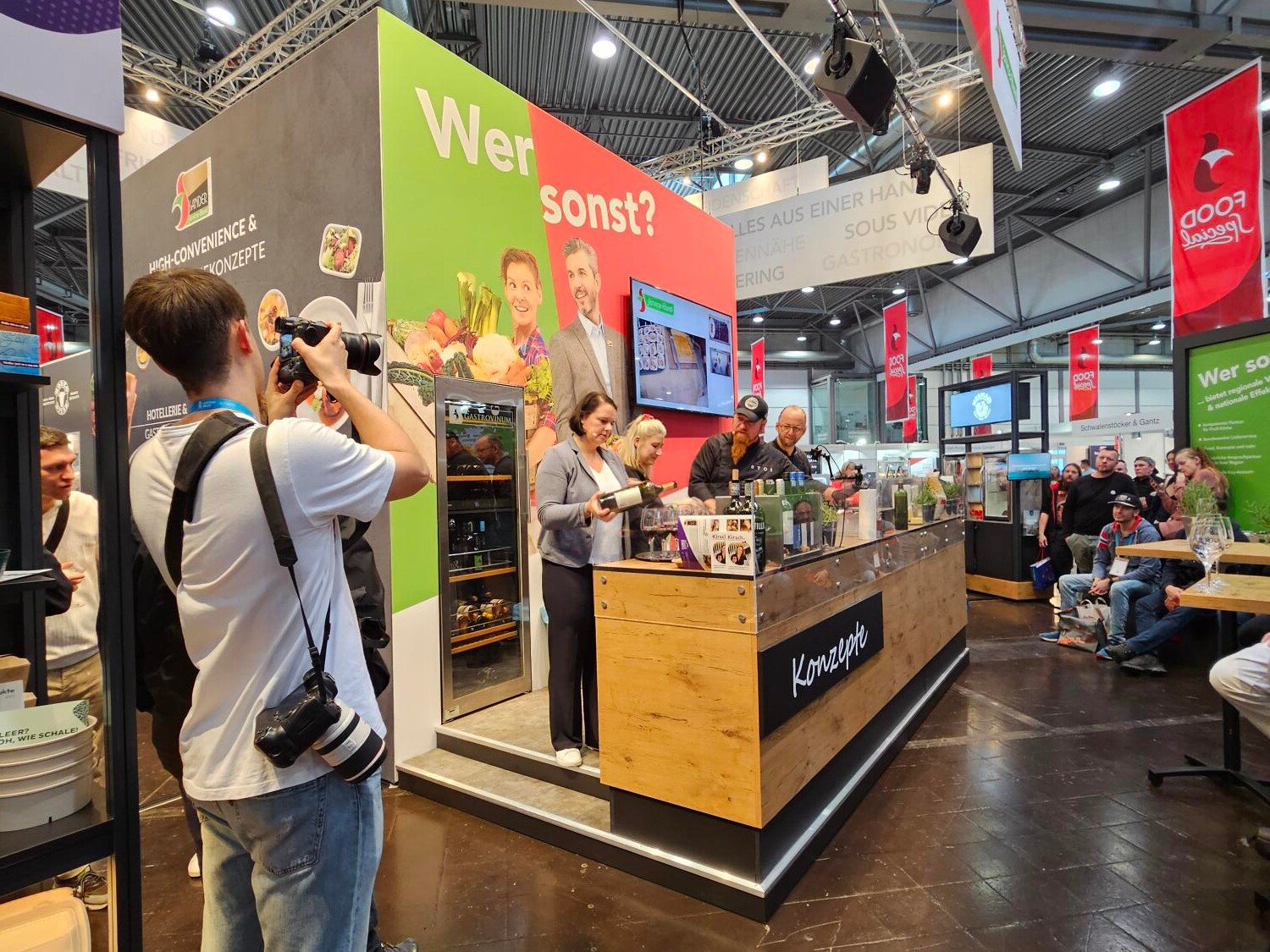 riationen Eine Gruppe von Menschen in einem Raum, darunter Männer und Frauen, die stehen und miteinander interagieren.