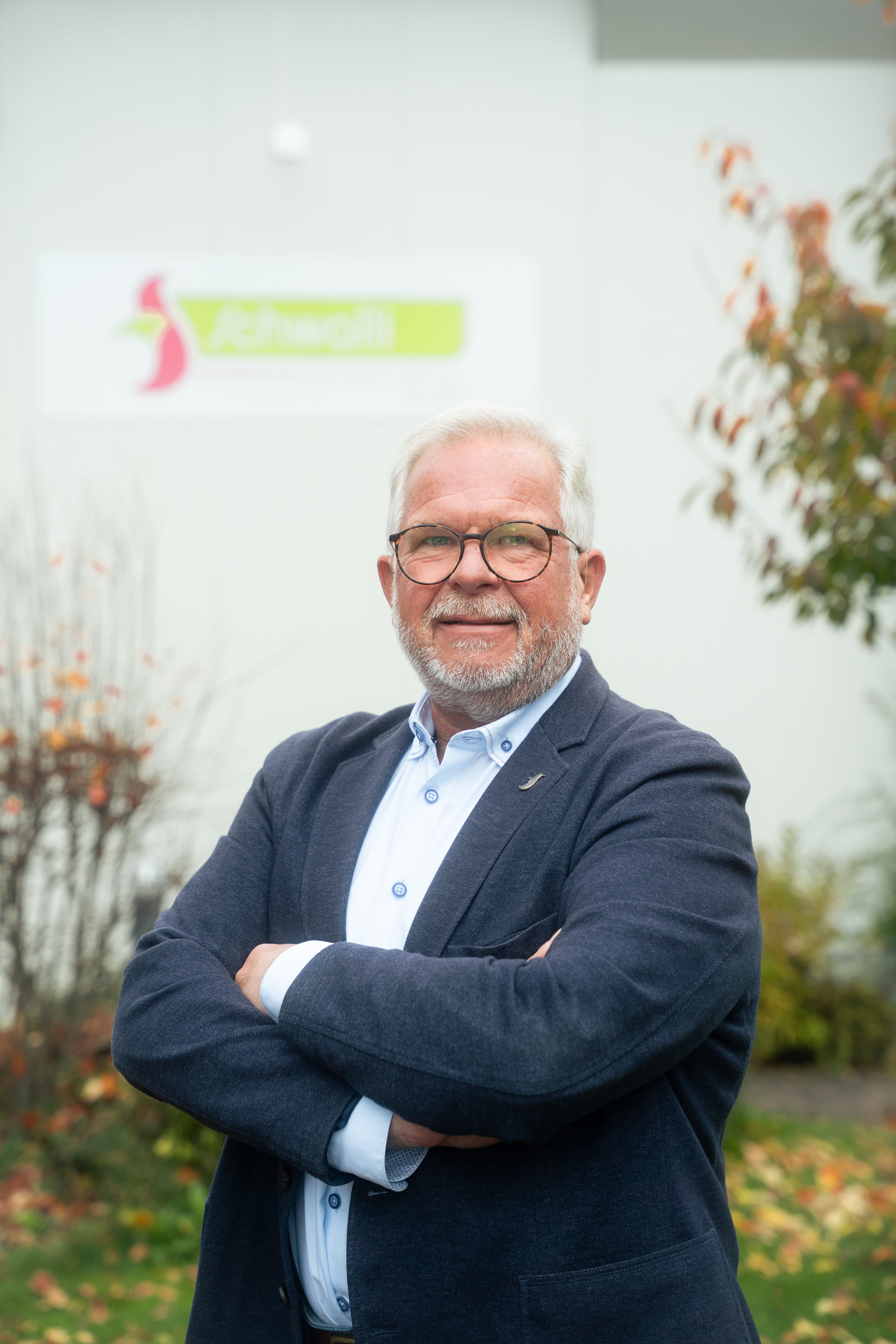 Ein Mann mit weißen Haaren und Bart, der eine Brille und ein Sakko trägt.