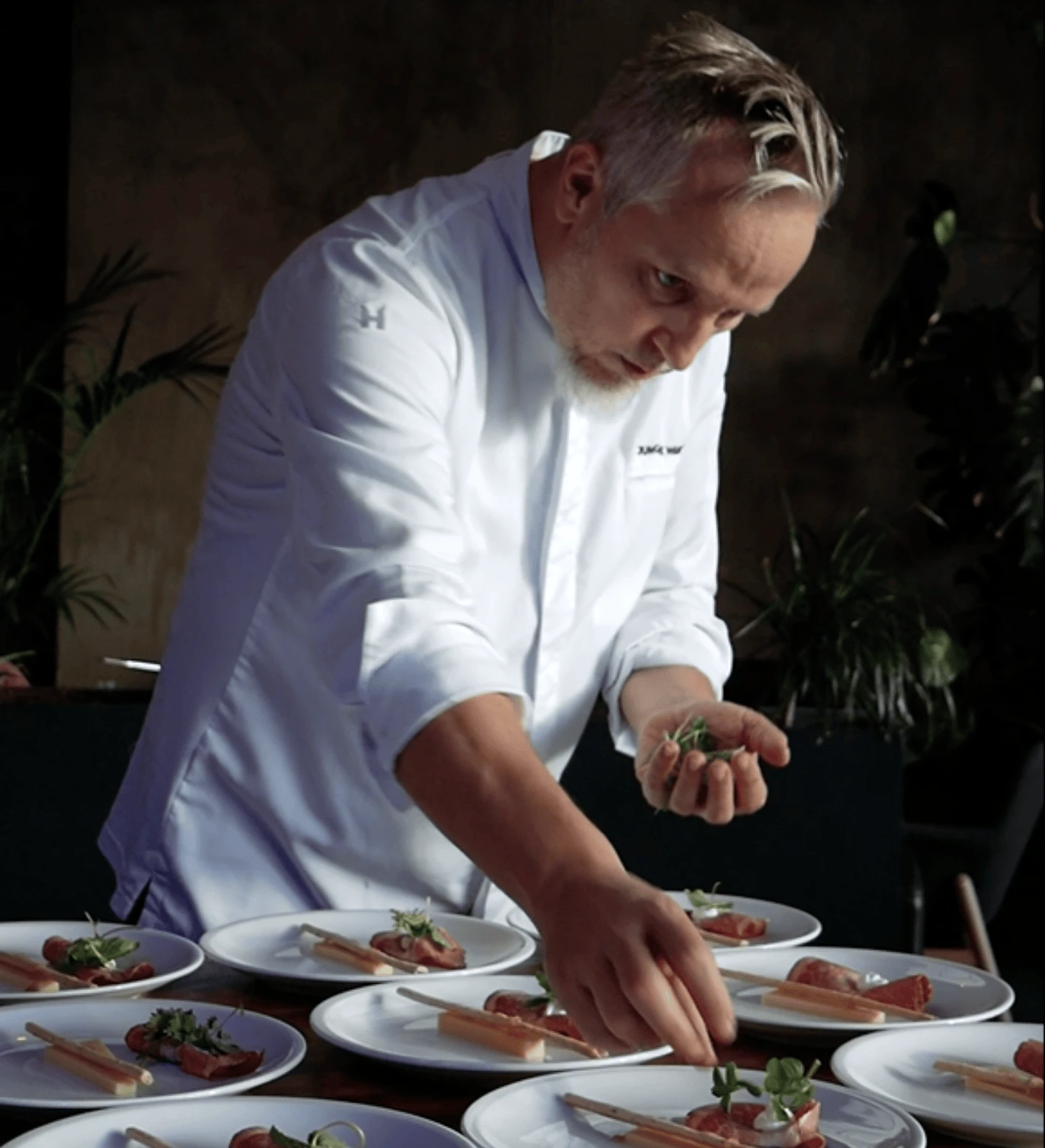 Ein Mann in einem weißen Hemd mit Tischgeschirr und Essen auf einem Tisch.