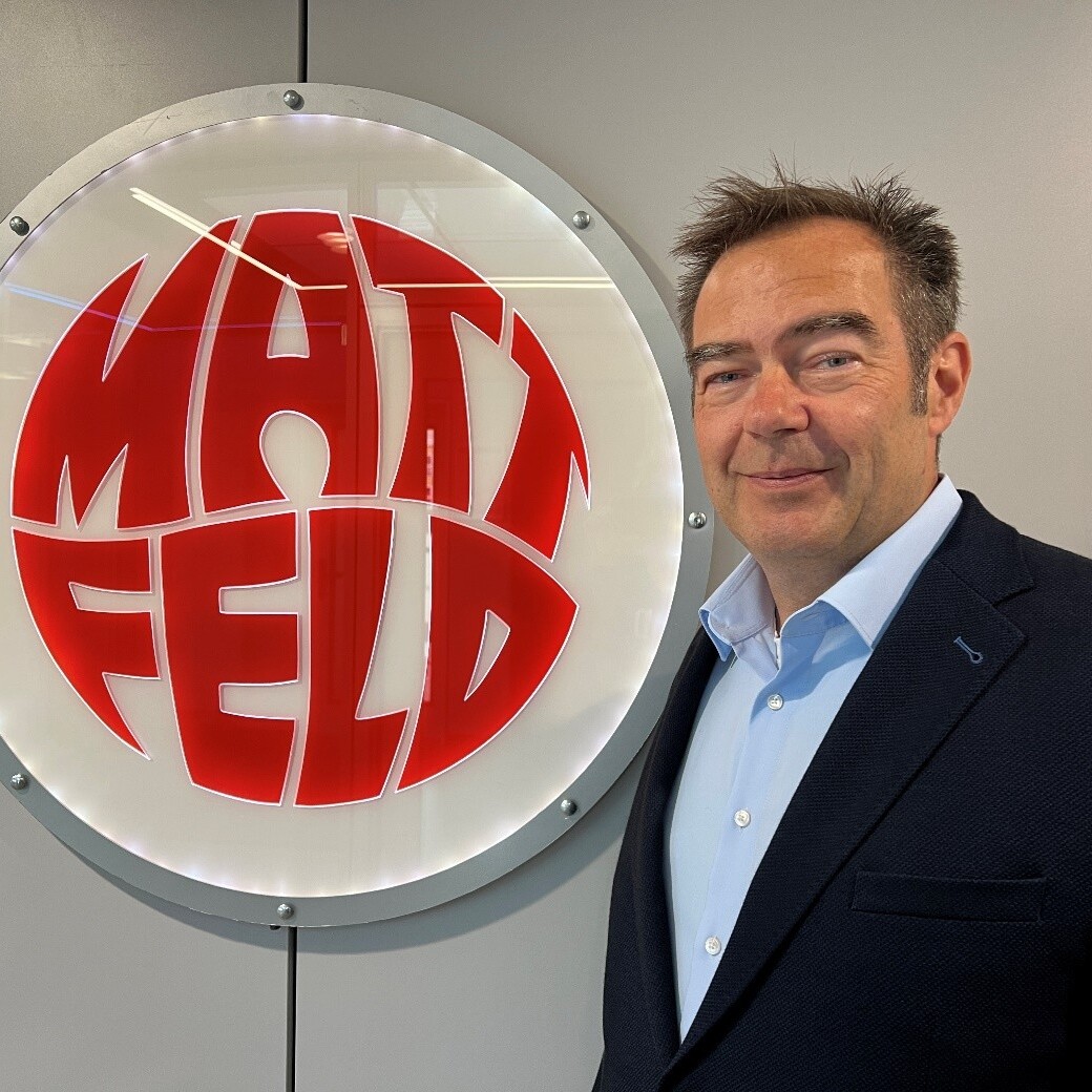 Matthias Rudolph Ein Mann im Anzug lächelt vor einem Schild.