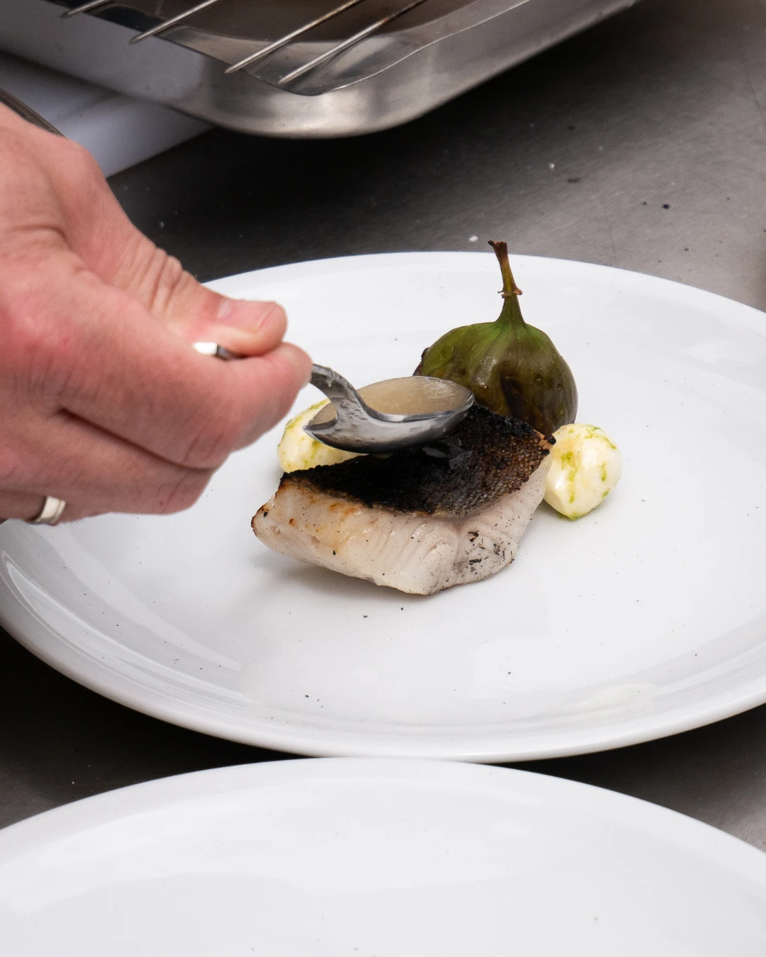 Eine Person hält einen Löffel über ein Stück Fisch.