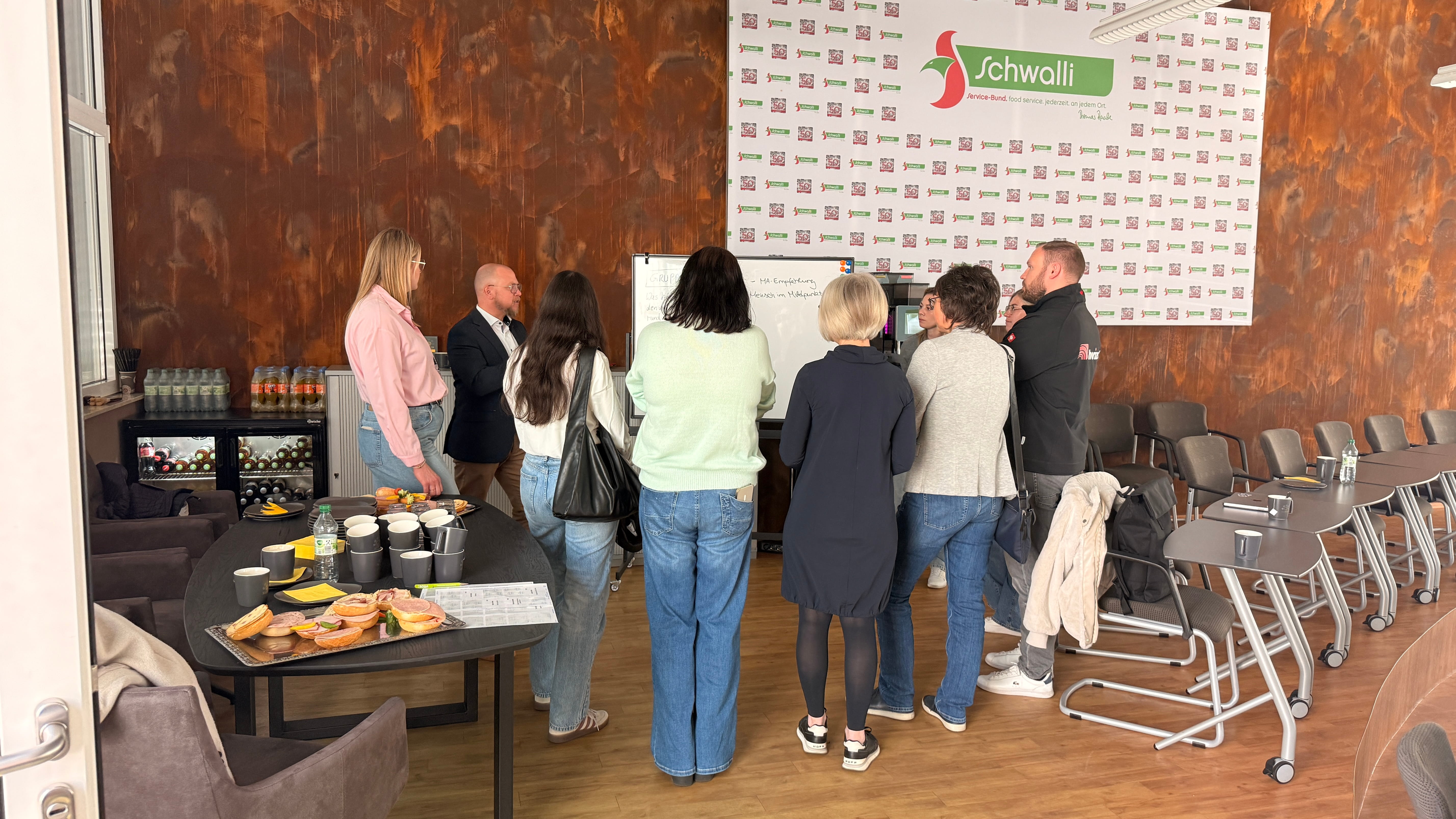 Eine Gruppe von Menschen steht vor einem Whiteboard.