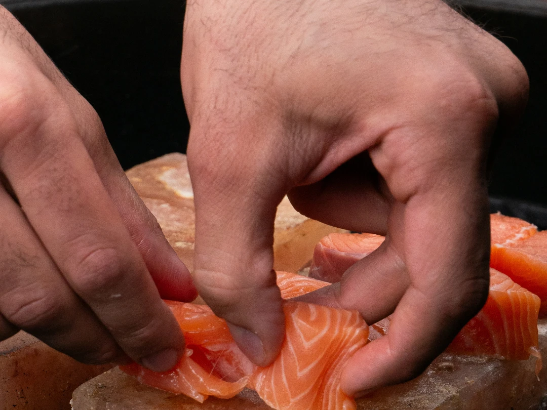 Eine Person kocht Lachs auf einem Salzstein vom Grill.